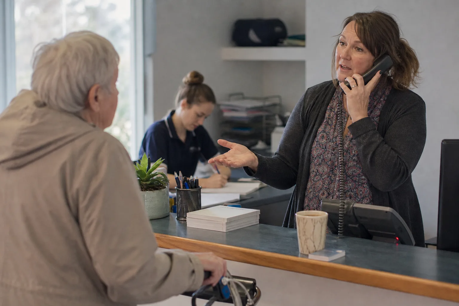 Receptionist at a Melbourne physio clinic juggling calls while a colleague books a qualified lead, showing voice AI vs human lead qualification