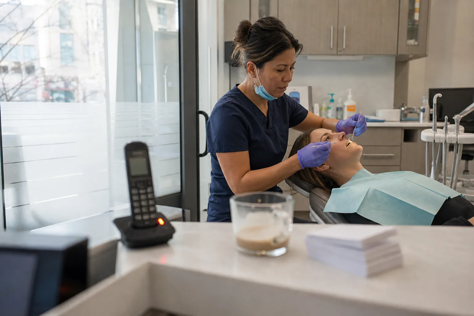 Dentist treating patient while phone rings at front desk, showing need for virtual receptionist services