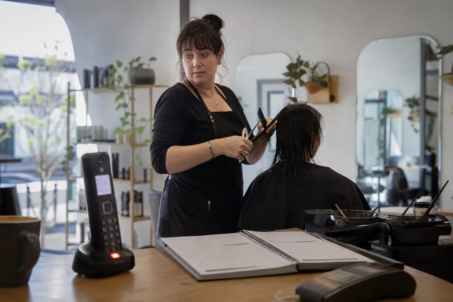 Auckland salon owner mid-haircut glances at a ringing phone on the counter, a booking about to be missed